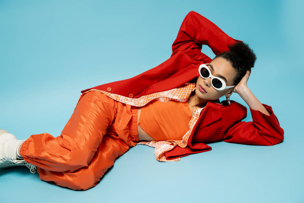unique style, expressive african american model in trendy vibrant outfit lying on blue background - Photo, Image