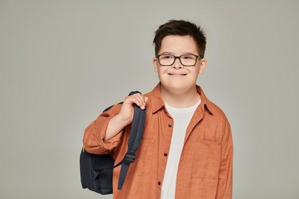Zihinsel engelli kaygısız okul çocuğu gri, down sendromu konseptine sırt çantası tutuyor. - Fotoğraf, Görsel