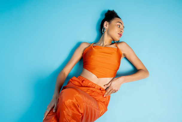 stylish attractive woman posing on floor wearing catchy bright attire and hoop earrings looking away - Photo, Image