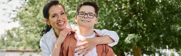 sorridente donna di mezza età che abbraccia il figlio con sindrome di Down nel parco, connessione emotiva, striscione - Foto, immagini