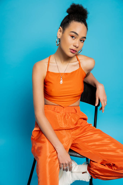close up fashion model in orange stylish wear and vivid makeup sitting and looking at camera - Фото, изображение
