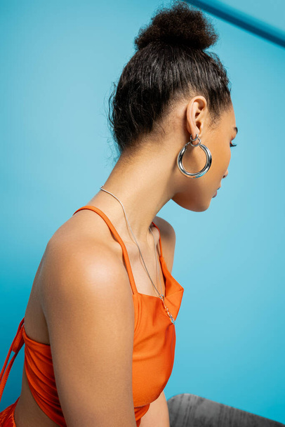 trendy Afrikaans Amerikaans fashion model in opvallende oranje outfit met hoepel oorbellen op zoek weg - Foto, afbeelding