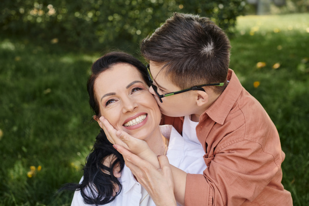 preteen αγόρι με σύνδρομο down, σε γυαλιά, φιλιά περιχαρής μητέρα στο πάρκο, άνευ όρων αγάπη - Φωτογραφία, εικόνα
