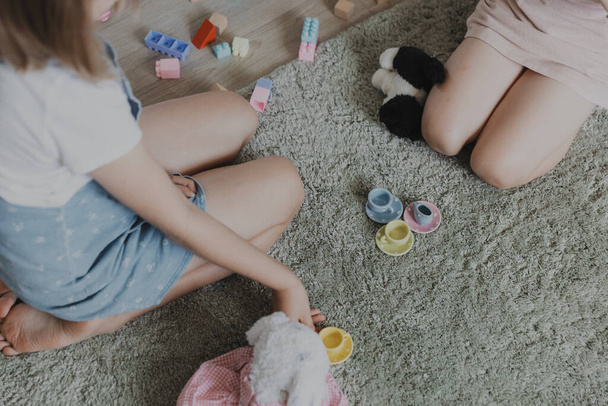 Дети играют чаепитие с красочным керамическим набором кухни. Дети, сидящие на ковре в домашней спальне, детской игровой комнате, игровой площадке, игровом центре. Образовательные экологически чистые детские игры - Фото, изображение