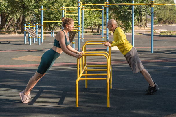 Egy fiatal nő és egy férfi fekvőtámaszt csinálnak egy fém szimulátoron egy utcai sportpályán. Egészséges életmód - Fotó, kép