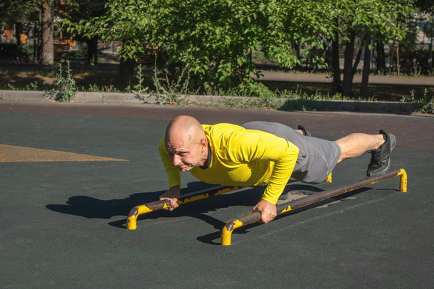 Paralel barlarda şınav çeken bir adam güneşli bir yaz gününde açık hava spor sahasında egzersiz yapıyor. Sağlıklı yaşam tarzı - Fotoğraf, Görsel