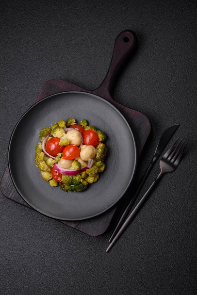 Ensalada fresca deliciosa con brócoli, tomates cherry, champiñones, cebollas, sal, especias y hierbas sobre un fondo de hormigón oscuro - Foto, imagen