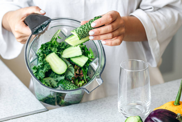 Healthy eating, cooking, vegetarian food, dieting and people concept, close up of woman with blender chopping green vegetables for detox shake or smoothie at home. - Photo, Image