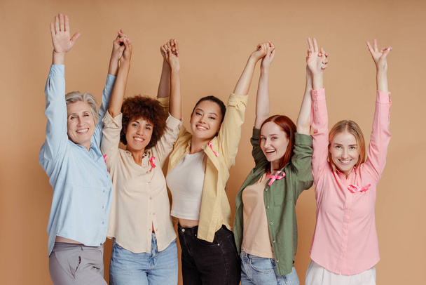 Las mujeres multiétnicas que usan cinta rosa levantando las manos celebran la recuperación. Concientización sobre el cáncer de mama - Foto, imagen