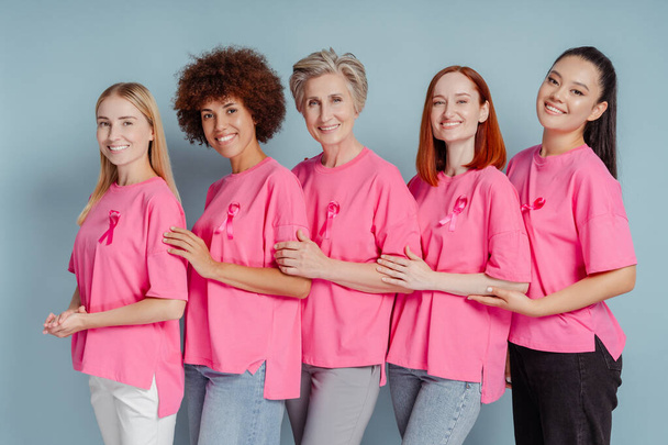 Groep van lachende vrouwen met roze lint knuffelen geïsoleerd op de achtergrond. Bewustwording van borstkanker - Foto, afbeelding