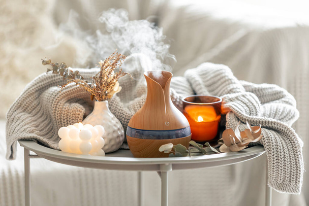 Composizione di aroma con un diffusore di olio di aroma moderno, candele e un elemento lavorato a maglia in interno di camera. - Foto, immagini