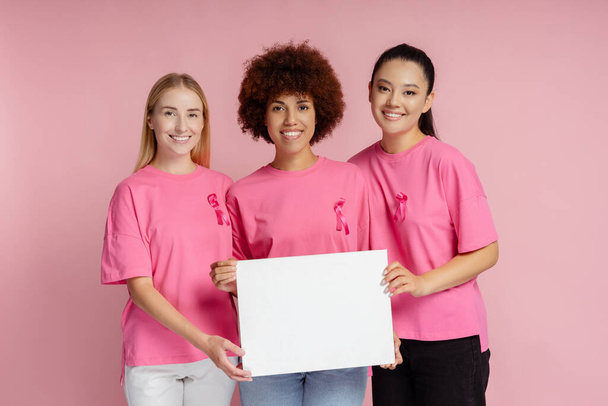 Lächelnde Frauen mit Brustkrebs rosa Schleife hält leeres Brett isoliert auf rosa Hintergrund, Attrappe - Foto, Bild
