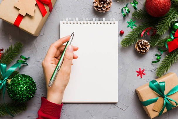 Kobieta pisząc Boże Narodzenie zrobić listę na notatniku na kolorowe tło z dekoracjami xmas. - Zdjęcie, obraz