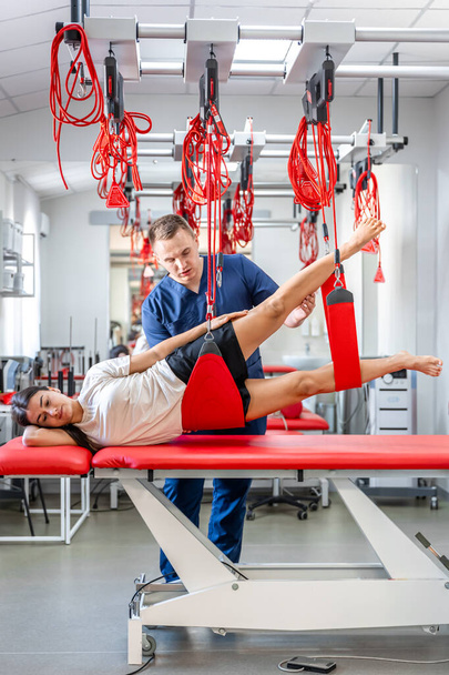 Pacjentka wisząca na zawieszeniu w ośrodku rehabilitacyjnym, ćwiczenia terapeutyczne i aktywacja nerwowo-mięśniowa na zawiesinach czerwonego sznurka, technika neuracka. - Zdjęcie, obraz