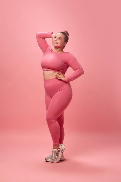 Full length happy young attractive plus size active woman in pink top and legging posing looking away isolated studio background. Concept of workout, sport, motivation body positivity - Fotografie, Obrázek