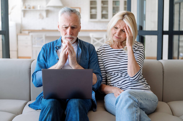 Zdenerwowana para patrząca na ekran komputera w domu. Szokujące złe wieści, czytanie wiadomości e-mail lub rozmowa przez połączenie wideo. Sfrustrowany mąż i żona - Zdjęcie, obraz