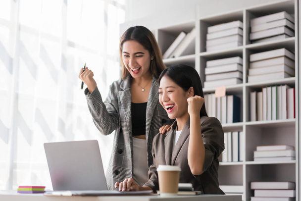 Deux femmes d'affaires lit les données financières sur ordinateur portable et lever le bras pour célébrer avec succès entreprise. - Photo, image