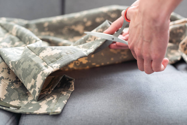 Professionele kleermaker snijden camouflage stof met schaar in de werkplaats, close-up. Hoge kwaliteit foto - Foto, afbeelding
