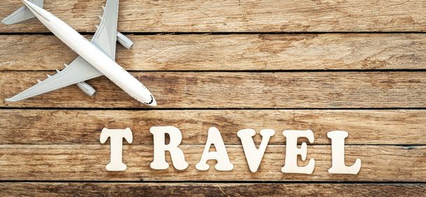 Word Travel and airplane on wooden background, top view. - Photo, Image