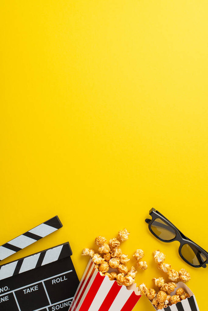Cinematograph concept visualized: Vertical top view of striped containers, holding popcorn, 3D glasses, and a clapperboard. Presented on yellow canvas with vacant space for text or promotional content - Photo, Image