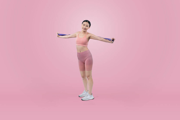 Krachtige energieke vrouw in sportkleding portret stretching weerstand sport band. Jonge atletische aziatische vrouw kracht en uithoudingsvermogen training sessie training routine concept op geïsoleerde achtergrond. - Foto, afbeelding