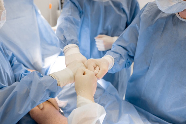 Chirurdzy podają sobie ręce po udanej operacji na sali operacyjnej. Koncepcja pracy zespołowej i sukces w chirurgii - Zdjęcie, obraz