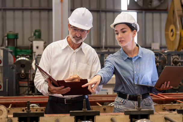 Inżynier fabryki z asystentem przy użyciu laptopa do przeprowadzania inspekcji maszyn przemysłowych ze stali, co stanowi przykład przywództwa jako nadzorca inspekcji maszyn w produkcji wyrobów metalowych. - Zdjęcie, obraz