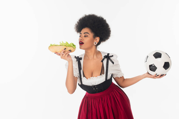 african american bavarian waitress with mug of beer opening mouth near tasty hot dog on white - Foto, immagini