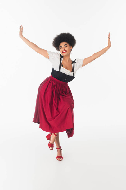 радісна афроамериканська баварська офіціантка в елегантному дирндлі виконує танець на білому - Фото, зображення