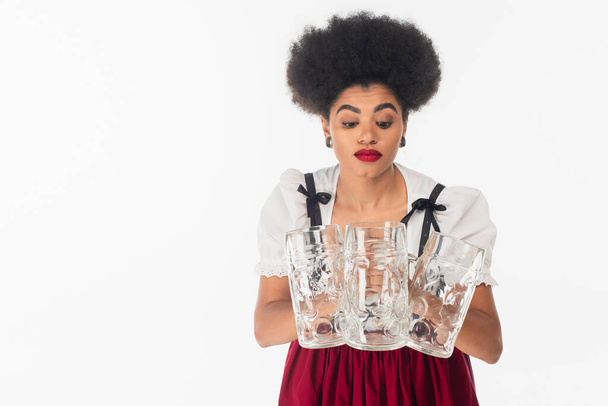 discouraged african american bavarian waitress in oktoberfest outfit with empty beer mugs on white - Photo, Image