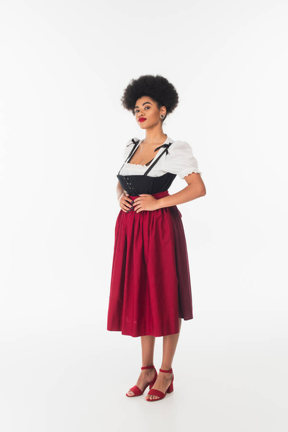 confident african american oktoberfest waitress in traditional bavarian costume standing on white - Foto, afbeelding