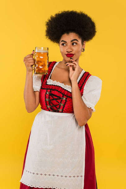 tricky african american oktoberfest waitress in dirndl costume standing with beer mug on yellow - Foto, Bild