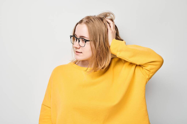 Clever blond student girl with glasses touches head thinks, chooses isolated on white studio background with copy space. Confidence smart genius - Photo, image