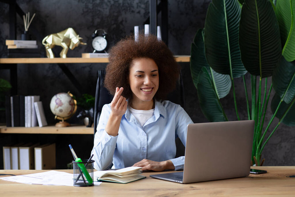 アフリカ系アメリカ人女性は,現代のオフィスでラップトップでオンラインで話しながら,指で愛のジェスチャーを示しています, オフィスの若いビジネス女性  - 写真・画像