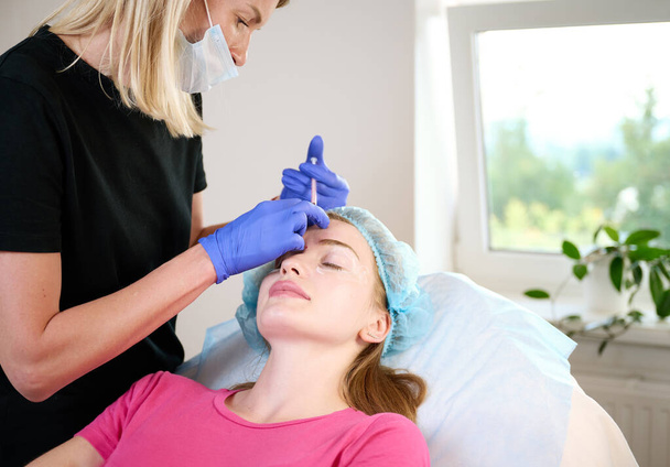 Kosmetolog wstrzykuje substancję pacjentom modyfikującym twarz w celu dokonania korekcji niechirurgicznej. Zastrzyki wypełniacza. Koncepcja zabiegów estetycznych. - Zdjęcie, obraz