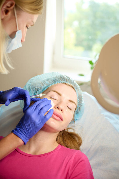 Cosmetoloog injecteert substantie in het gezicht van de patiënt om niet-chirurgische correctie te maken. Vulinjecties. Esthetische correctieve behandelingen concept. - Foto, afbeelding