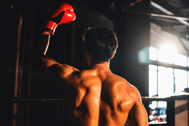 Vista trasera del victorioso boxeador Muay Thai golpea pose triunfante, disfrutando de la gloria de su victoria duramente ganada mostrando orgullosamente su cuerpo fuerte y musculoso. Impulso - Foto, Imagen