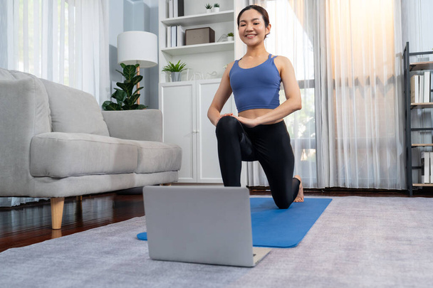 Spor kıyafetli Asyalı bir kadın spor salonunda antrenman yaparken spor minderinde yoga yapıyor. Sağlıklı vücut bakımı kadın dizüstü bilgisayardan yoga videosu izliyor. Kuvvetli - Fotoğraf, Görsel