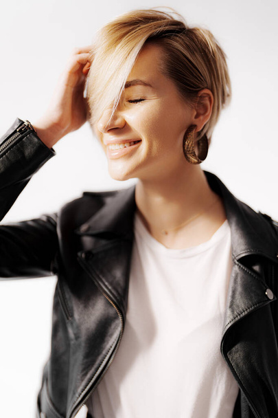 A happy blonde woman in a leather jacket on white background. The woman has her eyes closed, fair skin, and short straight hair. She looks shy and cheerful - Photo, Image