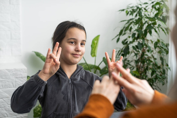Schattig klein meisje maken hand gebaar leren gebarentaal met mam of vrouwelijke oppas, glimlachend klein kind praktijk non-verbale praten met leraar thuis, kleuter gehandicapt kind hebben les met tutor. - Foto, afbeelding