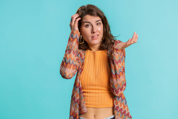 I dont know what to say. Confused Caucasian woman feeling embarrassed about ambiguous question, having doubts, no idea, being clueless and uncertain. Girl isolated on blue studio background indoors - Photo, Image