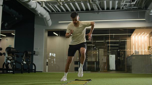 Professzionális labdarúgó férfi izmos lábak futtatni tornaterem használata sport felszerelés létra felmelegedés kardió edzés kitartás gyorsan rohanó férfi kaukázusi sportoló ugrás felkészülés futball mérkőzés - Fotó, kép