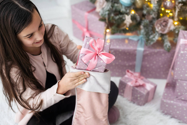 Fröhliches kleines Mädchen nimmt Geschenke von einer Weihnachtssocke entgegen. - Foto, Bild