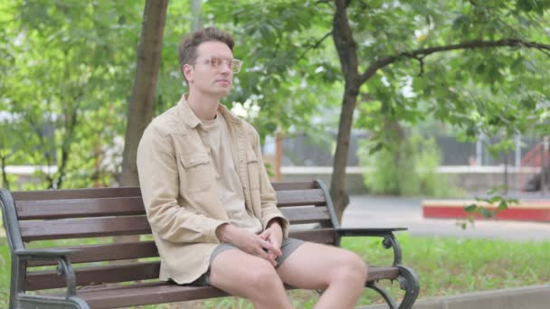 Σύγχρονος νεαρός άνδρας με πόνο στην πλάτη κάθεται στο Bench - Πλάνα, βίντεο