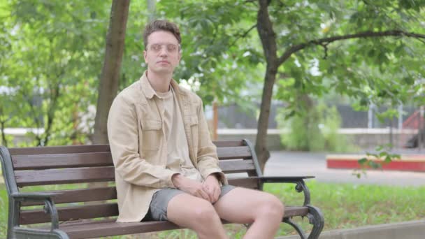 Nowoczesny młody człowiek stojący i wychodzący po siedzeniu na ławce - Materiał filmowy, wideo