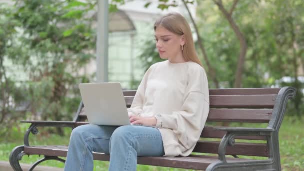 Случайная девушка улыбается перед камерой во время работы над ноутбуком на открытом воздухе - Кадры, видео