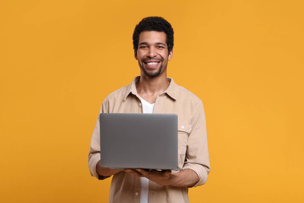 Happy man with laptop on orange background - Foto, imagen