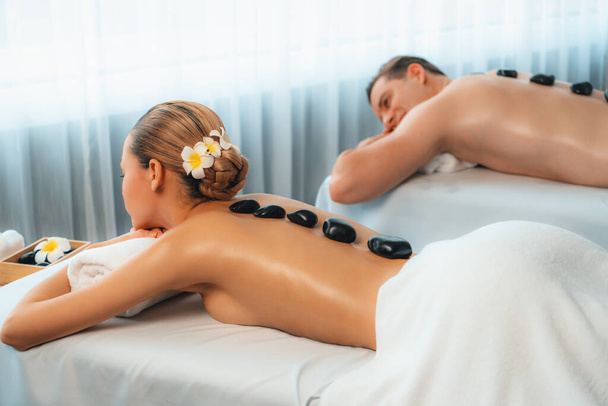 Hot stone massage in spa salon in luxe resort met daglicht sereniteit ambient, gelukzalig koppel klant genieten spa basalt steen massage glijden over het lichaam met rustgevende warmte. Stil maar. - Foto, afbeelding