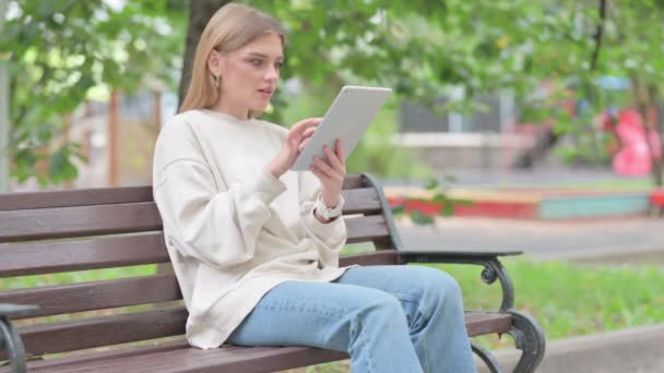 Mladá žena slaví na tabletu, zatímco sedí venku na lavičce - Záběry, video