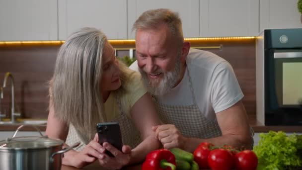 Смех на пенсии старые седые волосы кавказская семья влюбленная пара с помощью мобильного телефона онлайн заказ овощи питания на кухонный стол счастливая пожилая женщина и мужчина говорить покупки здоровое питание - Кадры, видео
